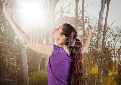 Woman arms in air against blurry trees with flare