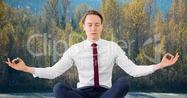 Business man meditating against trees