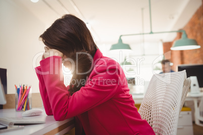 Tired female executive sitting with hands on forehead at desk