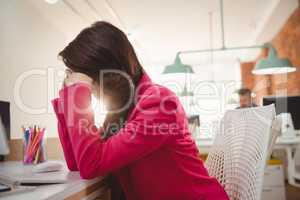 Tired female executive sitting with hands on forehead at desk