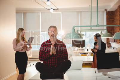 Male executive meditating on table in office