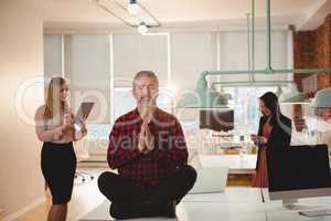 Male executive meditating on table in office