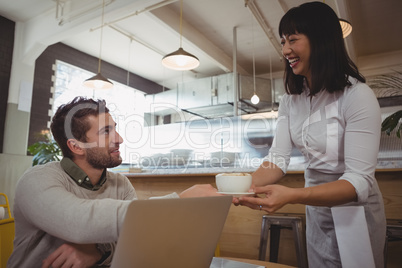 Smiling waitress serving coffee to man in cafe