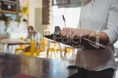 Mid section of waitress with clipboard in cafe