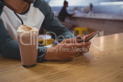 Mid section of man with milkshake glass using phone