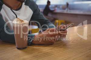 Mid section of man with milkshake glass using phone