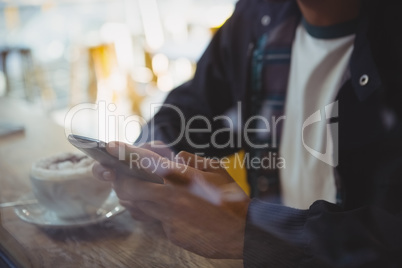 Mid section of man with coffee using phone in cafe