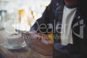 Mid section of man with coffee using phone in cafe