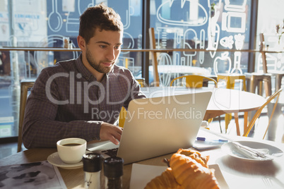 Businessman with breakfast using laptop in cafe