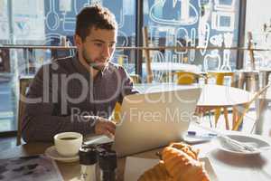 Businessman with breakfast using laptop in cafe