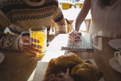 Mid section of woman with man writing on book in cafe