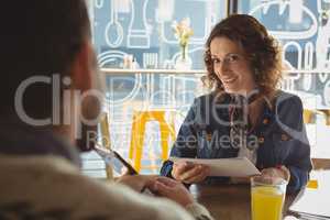 Smiling woman with document looking at man in cafe