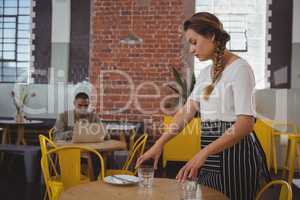Young waitress arranging glasses at table