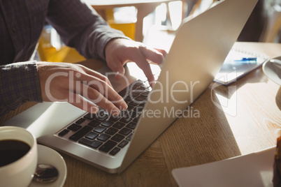 Cropped hands of businessman using laptop at table in cafe
