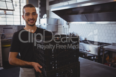 Portrait of smiling waiter holding crates in kitchen