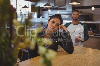 Bored woman at table with friend holding milkshake glasses in cafe