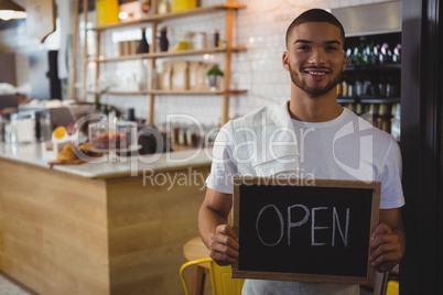 Portrait of waiter holding open sign in cafe