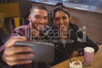 Smiling man with friend taking selfie in cafe