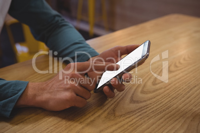 Cropped hands of man using phone at wooden table