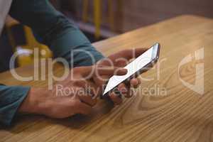 Cropped hands of man using phone at wooden table