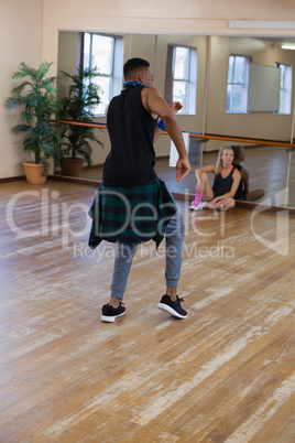 Male dancer rehearsing with friend sitting at studio
