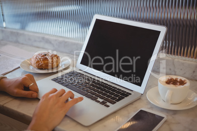 Cropped hands of woman using laptop in cafe