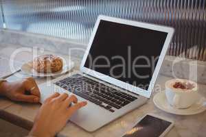 Cropped hands of woman using laptop in cafe