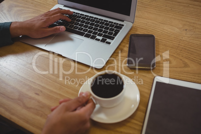 Cropped hands of man having black coffee while using laptop in cafe