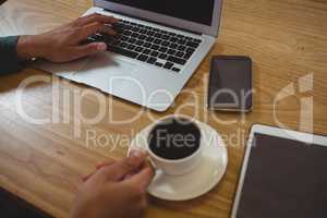 Cropped hands of man having black coffee while using laptop in cafe