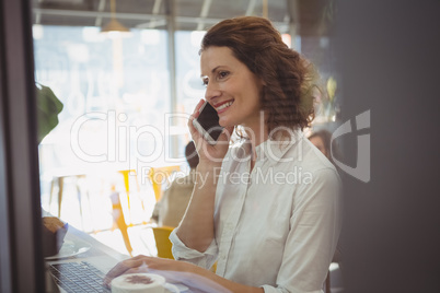 Woman using laptop while talking on phone in cafe