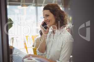 Woman using laptop while talking on phone in cafe