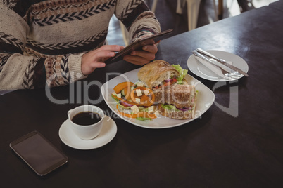 Mid section of man with breakfast using digital tablet in cafe Mid section of man with breakfast using digital tablet in cafe