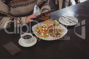 Mid section of man with breakfast using digital tablet in cafe