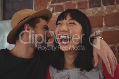 Man whispering in happy woman ear at cafe
