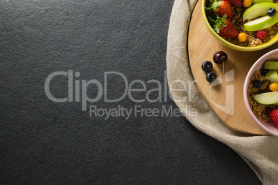 Bowls of breakfast cereals with fruits on chopping board