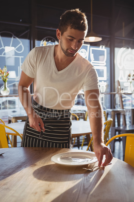 Waiter arranging utensils on table in cafe