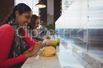 Woman with friend having burger in cafe