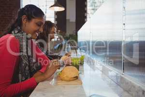 Woman with friend having burger in cafe