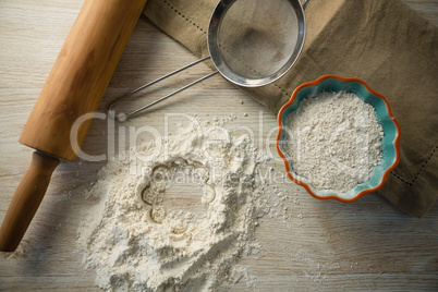 Overhead view of flour in bowl by rolling pin and strainer
