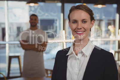 Portrait of female owner with waiter in background at cafe