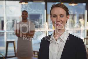 Portrait of female owner with waiter in background at cafe
