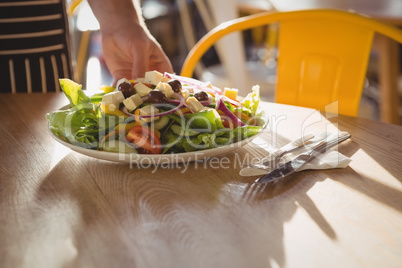 Cropped hand of waiter serving salad on table