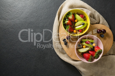 Bowls of breakfast cereals with fruits on chopping board