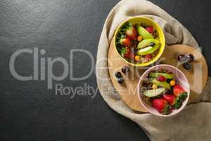 Bowls of breakfast cereals with fruits on chopping board