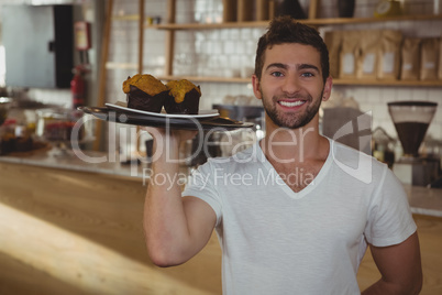 Portrait of waiter holding tray with muffins in cafe
