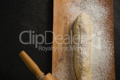 Raw loaf of bread with flour and rolling pin on cutting board