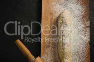Raw loaf of bread with flour and rolling pin on cutting board