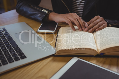 Mid section of woman with book and laptop in cafe