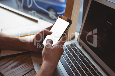 Cropped hand of man using mobile phone over laptop in cafe