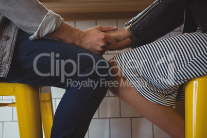 Mid section of couple holding hands on stool in cafe